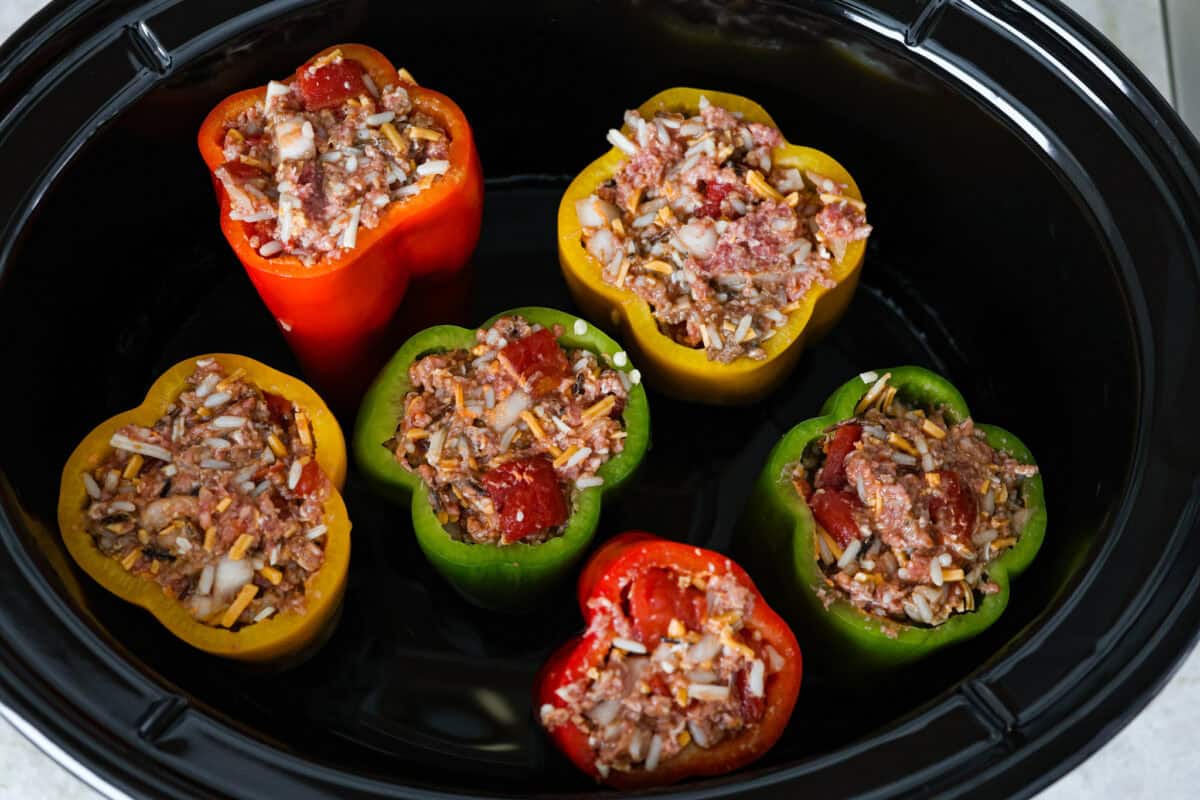 Slow cooker stuffed bell peppers are packed with ground beef, wild rice, diced tomatoes, soft black beans, and melty cheese. They cook to perfection in the slow cooker and make a healthy, delicious dinner your whole family will love! Overhead shot of stuffed bell peppers in slow cooker.