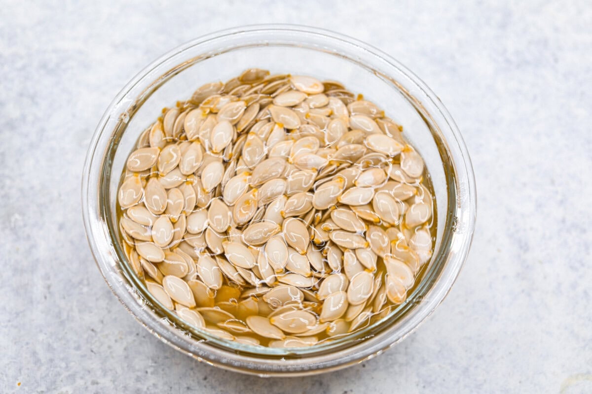 Crazy Good Roasted Pumpkin Seeds are a healthy and delicious snack you can enjoy while carving pumpkins this Halloween season. They are packed with essential vitamins and antioxidants that help you sleep better, boost your immune system, and promote heart health. Overhead shot ofseeds in a bowl of warm water.