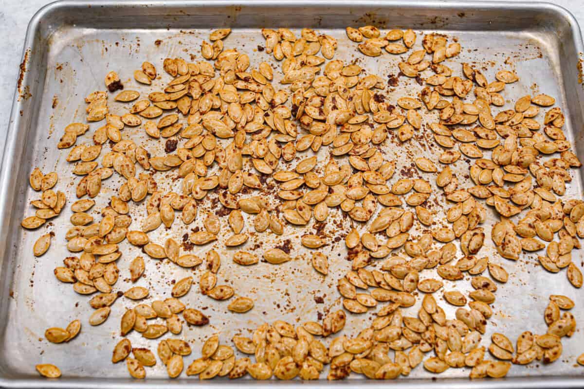 Crazy Good Roasted Pumpkin Seeds are a healthy and delicious snack you can enjoy while carving pumpkins this Halloween season. They are packed with essential vitamins and antioxidants that help you sleep better, boost your immune system, and promote heart health. Overhead shot of pumpkin seeds drenched in oil and seasonings.