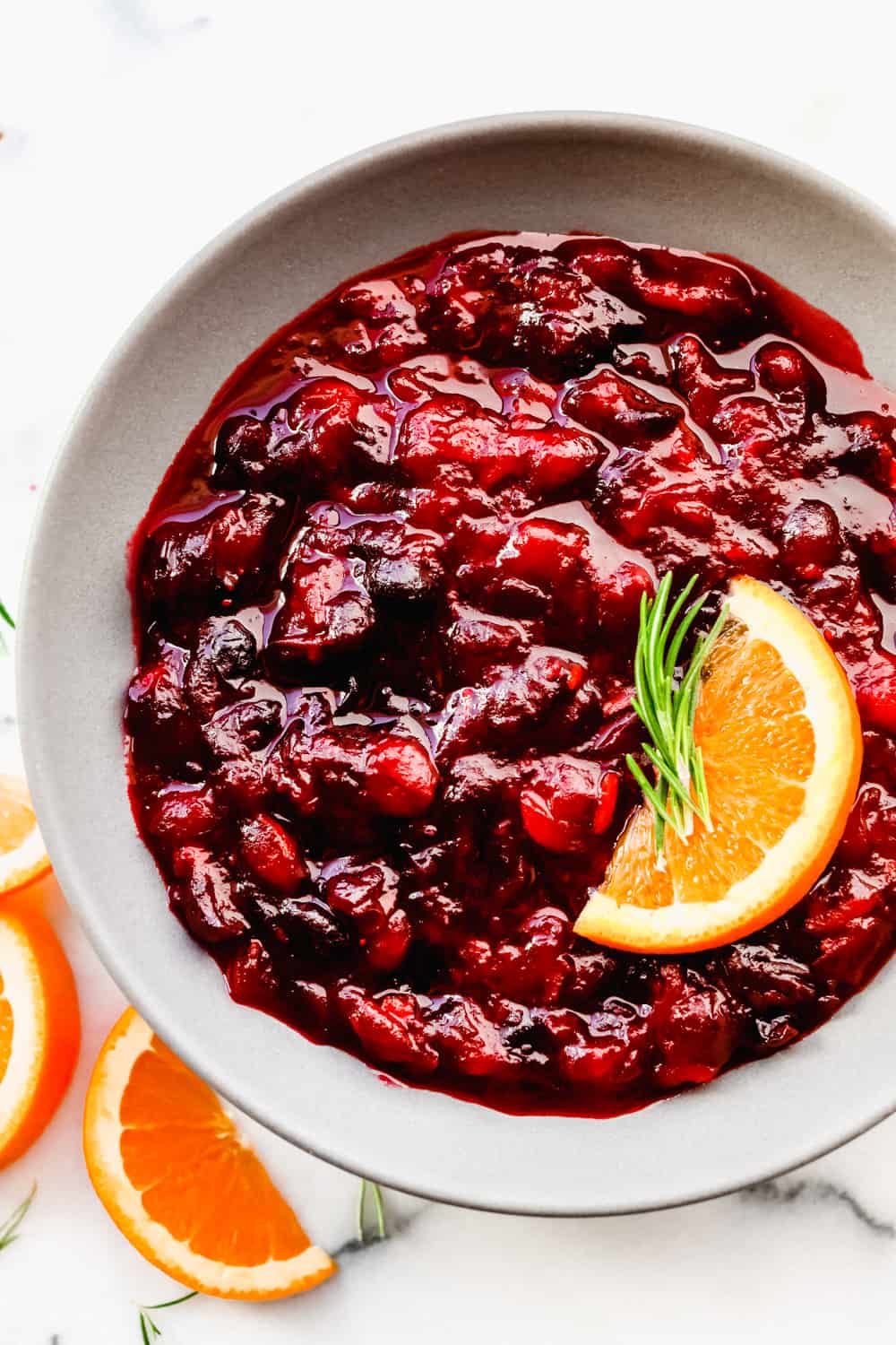 This cranberry sauce is the perfect mixture of sweet and tart! It's made with fresh cranberries and topped with orange zest to really set it apart! Cranberry sauce in a bowl with an orange slice.