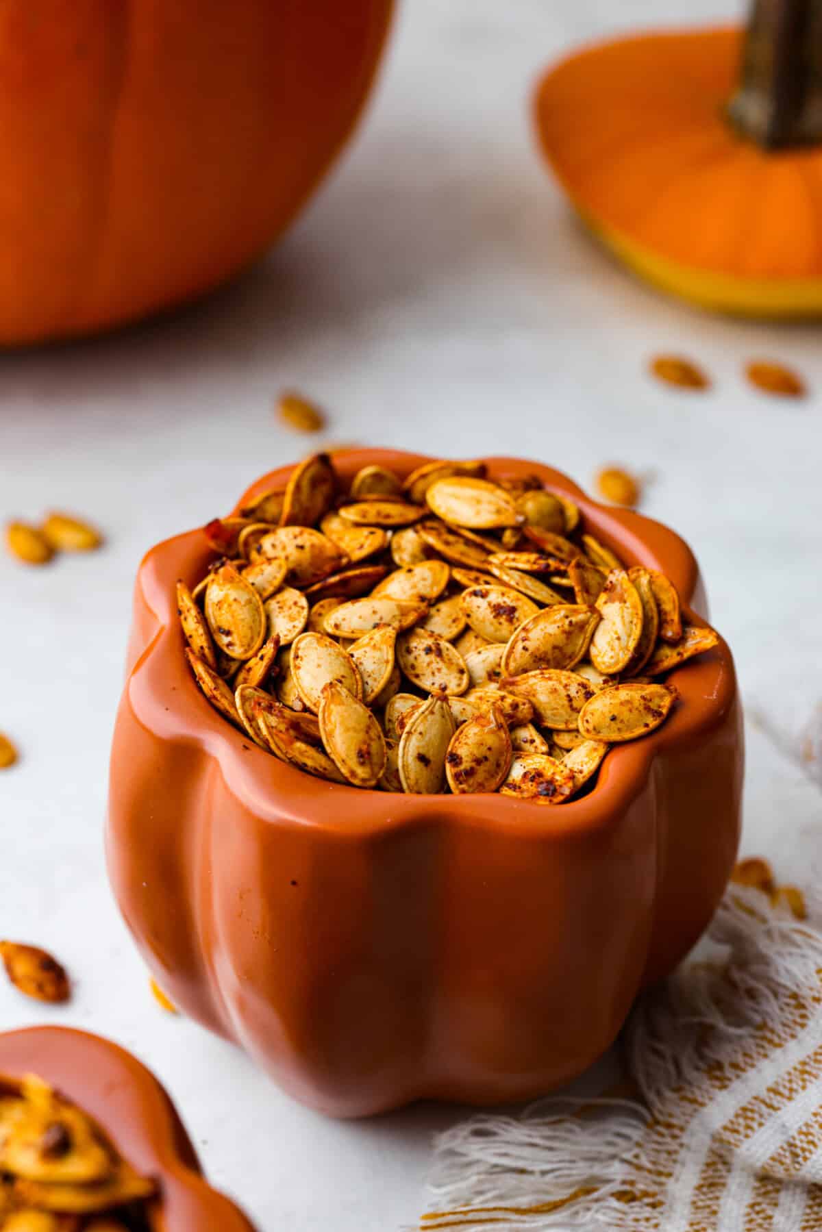 Crazy Good Roasted Pumpkin Seeds are a healthy and delicious snack you can enjoy while carving pumpkins this Halloween season. They are packed with essential vitamins and antioxidants that help you sleep better, boost your immune system, and promote heart health. Angle shot of roasted pumpkin seeds in a cute pumpkin container.