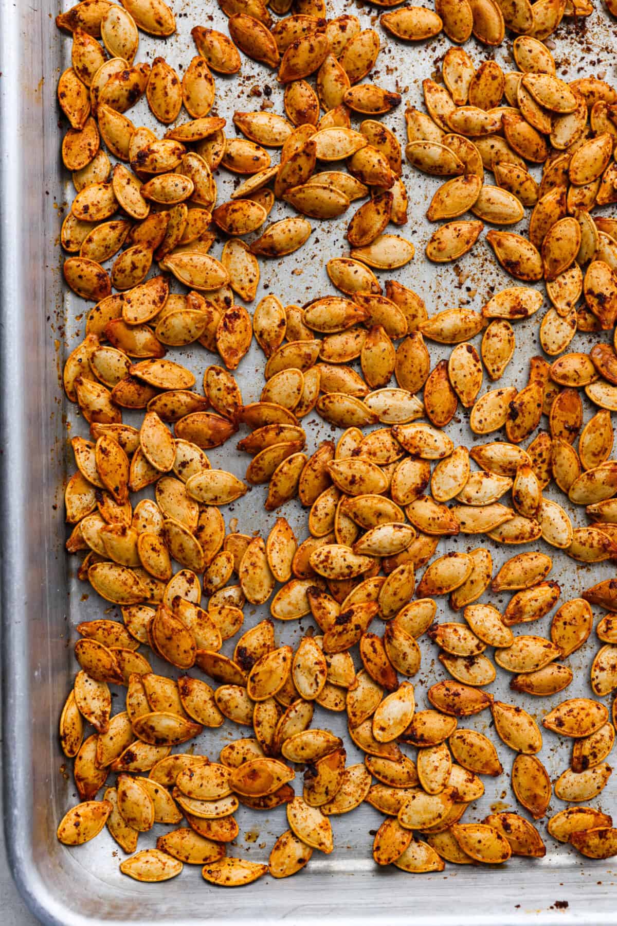 Crazy Good Roasted Pumpkin Seeds are a healthy and delicious snack you can enjoy while carving pumpkins this Halloween season. They are packed with essential vitamins and antioxidants that help you sleep better, boost your immune system, and promote heart health. Overhead shot of roasted pumpkin seeds on a pan.