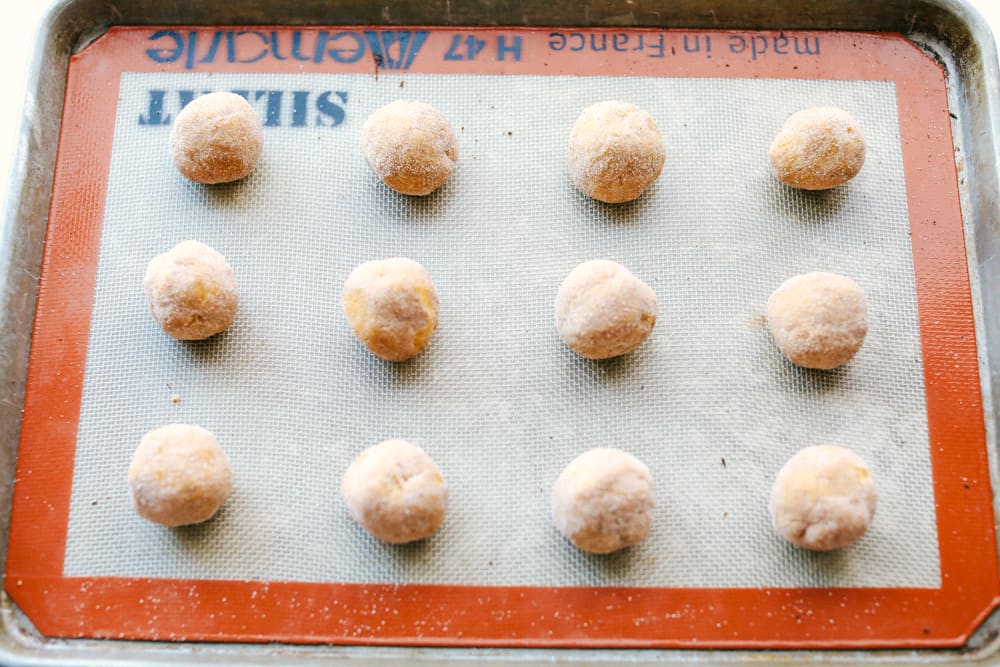Soft and Puffy Pumpkin Snickerdoodles are made with real pumpkin, fall seasonal spices mixed together and rolled with pumpkin pie spice and aย touch of sugar to add that extra sweetness and fallย flavor! This are a MUST make this fall season! dough rolled into balls on a cookie sheet