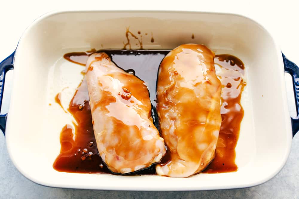 Easy Teriyaki Chicken Casserole isย a simple casserole made with the best homemade teriyaki sauce filled with vegetable stir fry, rice and baked to perfection. A savory dish everyone loves!ย Teriyaki sauce over chicken breast in a pan getting ready to be baked.