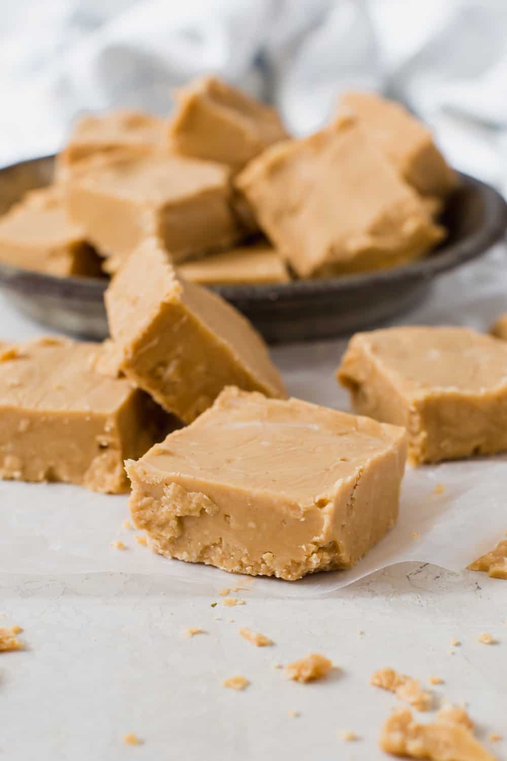 Creamy and smooth with a sweet peanut butter taste, this fudge is made with powdered sugar and butter for a deliciously soft and crumbly treat. Peanut Butter Fudge is a decadent dessert that is extremely easy to make. No candy thermometers and only five ingredients. pieces of peanut butter fudge on surface and in tin