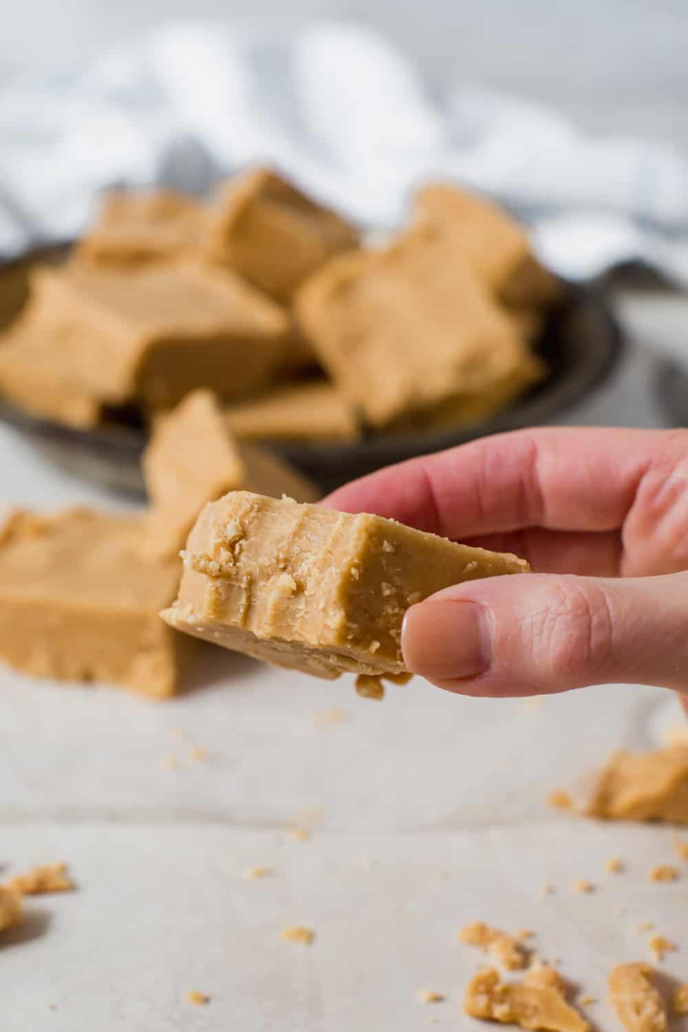 Creamy and smooth with a sweet peanut butter taste, this fudge is made with powdered sugar and butter for a deliciously soft and crumbly treat. Peanut Butter Fudge is a decadent dessert that is extremely easy to make. No candy thermometers and only five ingredients. hand holding piece of peanut butter fudge with bit taken out