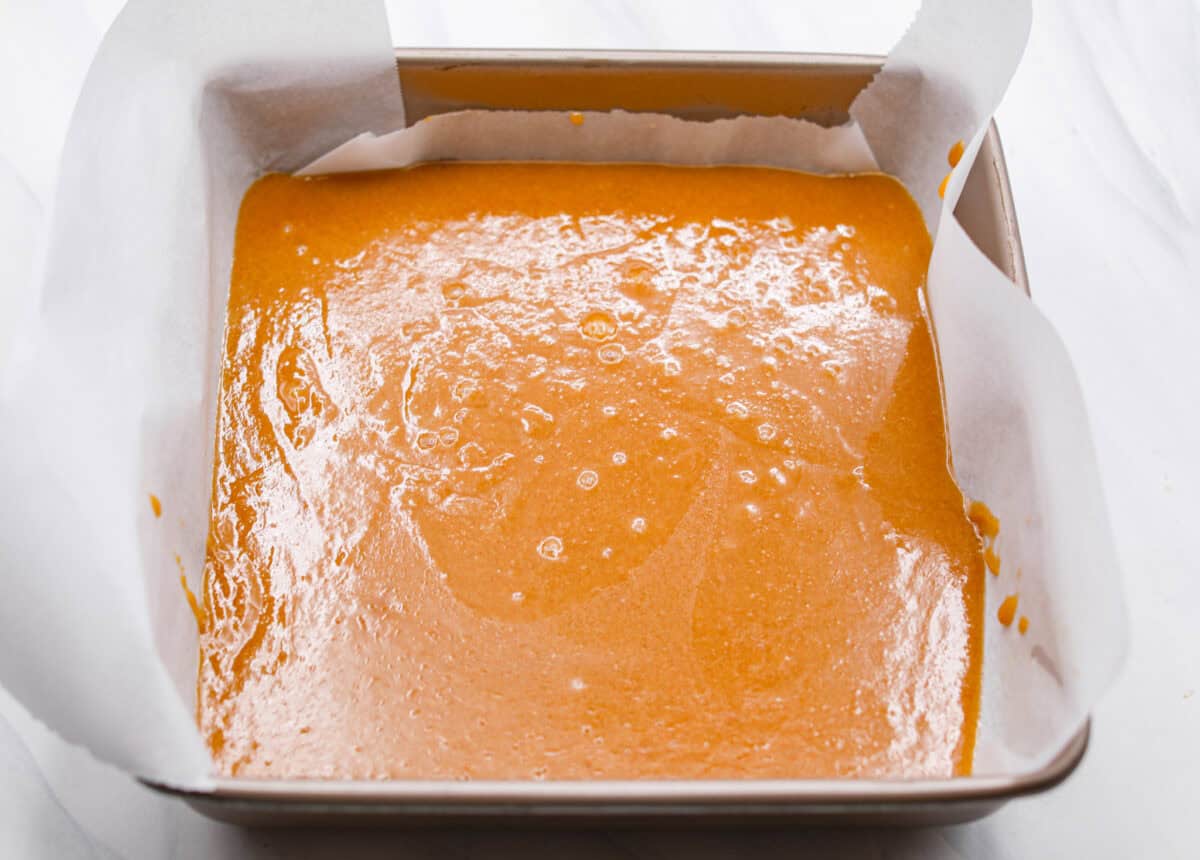 Homemade Caramels are perfectly buttery soft with just the right amount of sweet. They are easy to make and are the perfect neighbor gift for the holiday season. Overhead shot of a 9x9 pan with parchment paper and caramel poured into it.