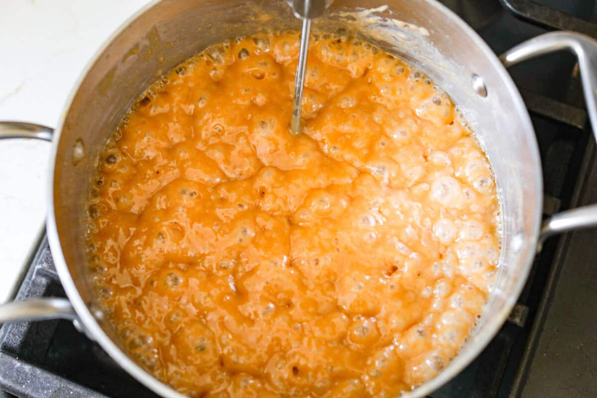 Homemade Caramels are perfectly buttery soft with just the right amount of sweet. They are easy to make and are the perfect neighbor gift for the holiday season. Overhead shot of pot with bubbling caramel and a candy thermometer sticking out of it.