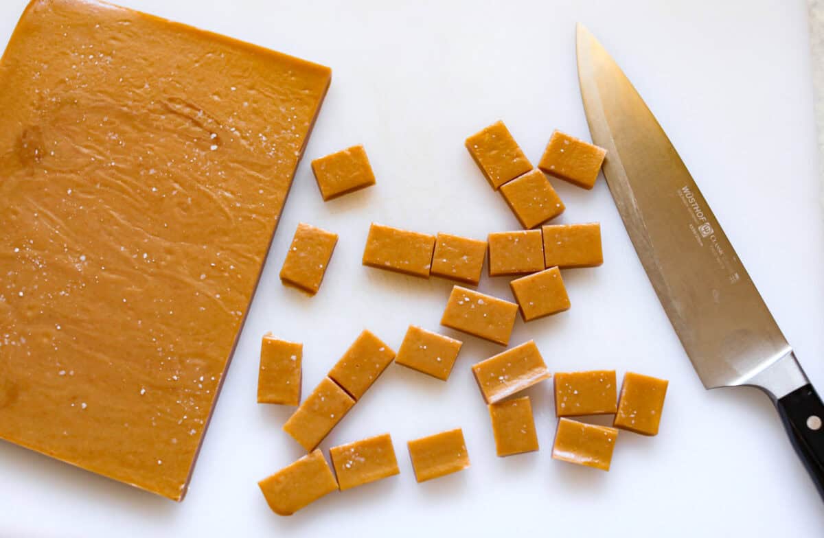 Homemade Caramels are perfectly buttery soft with just the right amount of sweet. They are easy to make and are the perfect neighbor gift for the holiday season. Overhead shot of cut up caramels next to the slab of caramel.