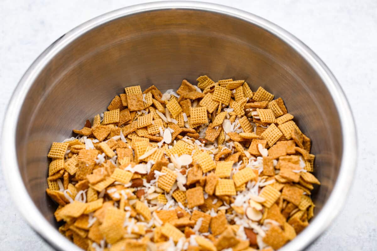 Ooey Gooey Chex Mix is the perfect sweet, salty, and crunchy blend. It has a mixture of cereal, sliced almonds, and shredded coconut, all covered in a soft caramel sugar mixture. This is a must-make for the holiday season! Overhead shot of cereal, coconut and almond mixture in a large bowl.