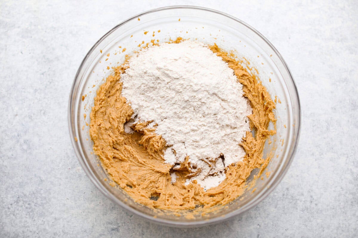 Peanut Butter Blossom Cookies are classic cookies that are perfect for every occasion. The delicious pairing of peanut butter and chocolate in these soft, buttery cookies will delight cookie lovers of all ages. Overhead shot of the wet ingredients with the dry ingredients dumped on top.