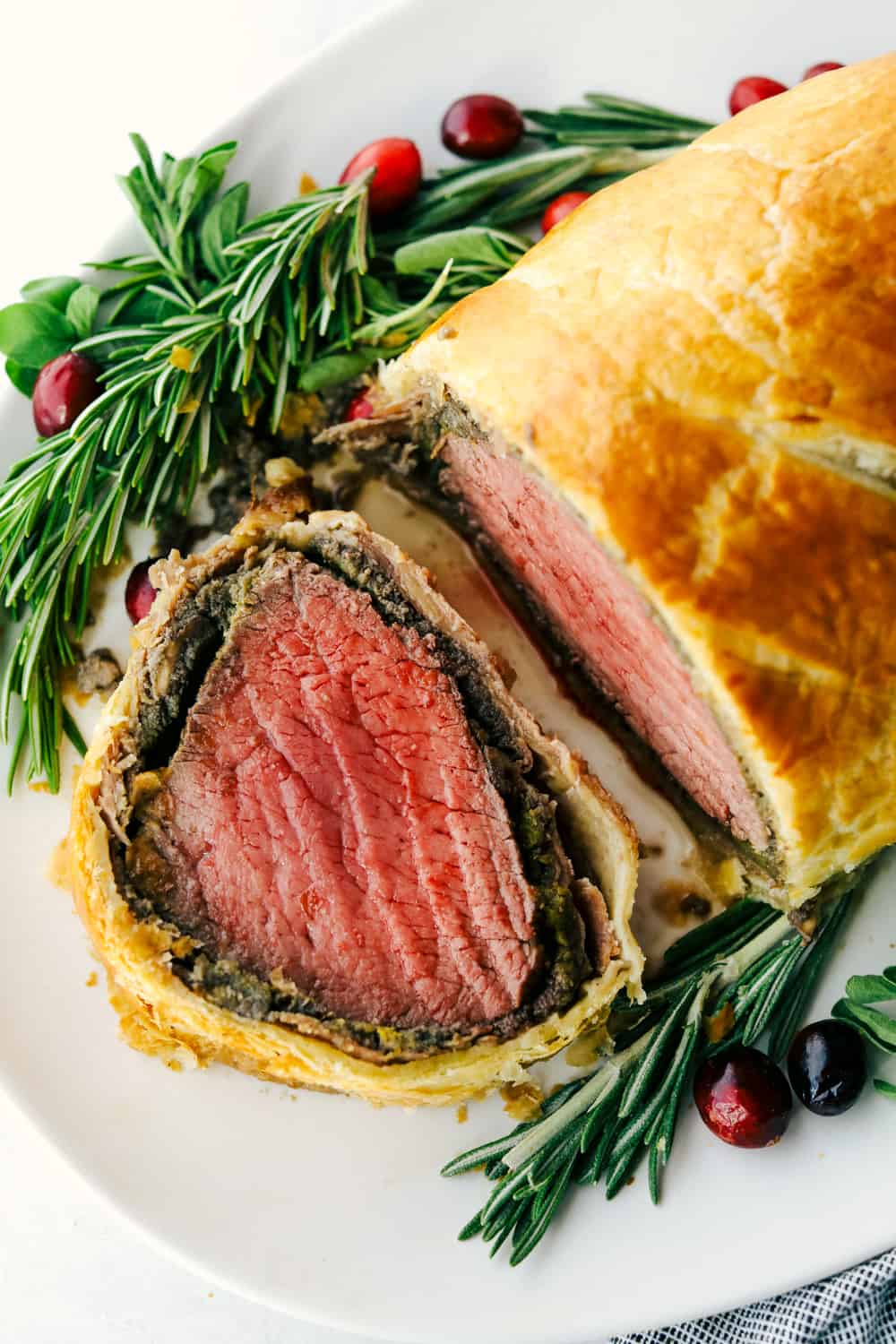 Best Ever Beef Wellington Recipe is a decadent tender and juicy beef tenderloin with a layer of mustard, mushroom sauce and prosciutto wrapped in a soft, buttery pastry that is cooked until golden brown. A holiday favorite! beef welling ton cut into a slice on a plate