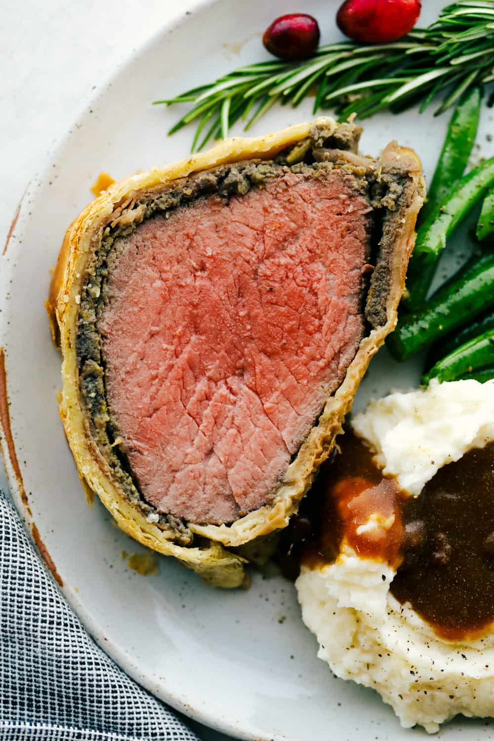 Best Ever Beef Wellington Recipe is a decadent tender and juicy beef tenderloin with a layer of mustard, mushroom sauce and prosciutto wrapped in a soft, buttery pastry that is cooked until golden brown. A holiday favorite! Beef Wellington sliced onto a plate with mashed potatoes and green beans