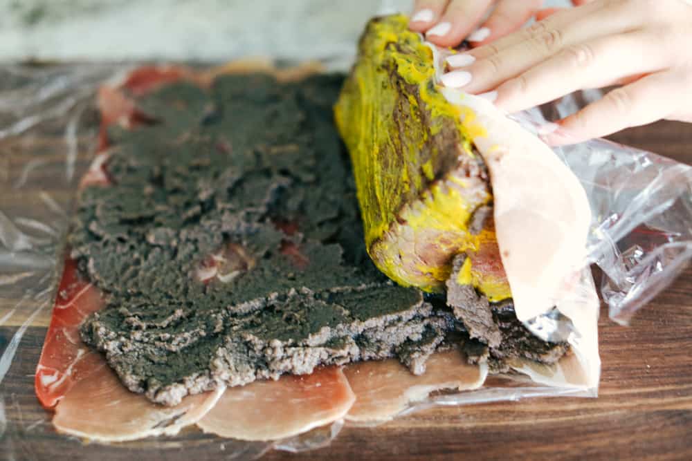 Best Ever Beef Wellington Recipe is a decadent tender and juicy beef tenderloin with a layer of mustard, mushroom sauce and prosciutto wrapped in a soft, buttery pastry that is cooked until golden brown. A holiday favorite! Beef being rolled into the mushroom and meat layers