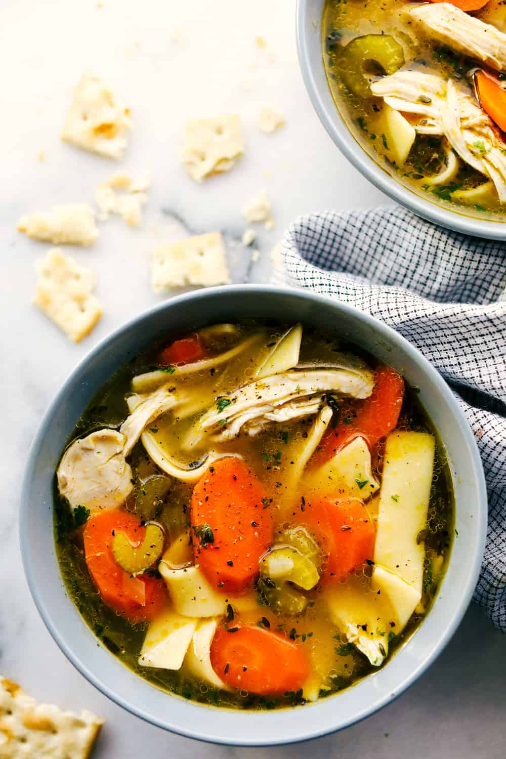 This is literally the BEST chicken noodle soup full of chicken, sliced carrots,ย celery, and tender wide noodles. A classic homemade soup seasoned and cooked to perfection. It's the perfect warm and comforting soup for the winter! Close view of chicken noodle soup in a gray bowl.