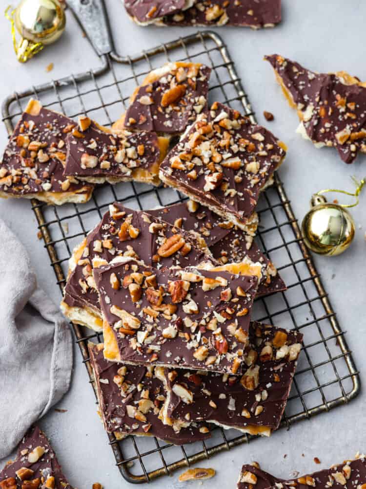 This is the Best Christmas Crack Recipe! It's a saltine cracker layered with toffee and creamy chocolate, then topped with crunchy pecans for the ultimate sweet and salty treat.ย This recipe is so easy, delicious, and addicting! Christmas crack broken up and sitting on top of a wire rack.