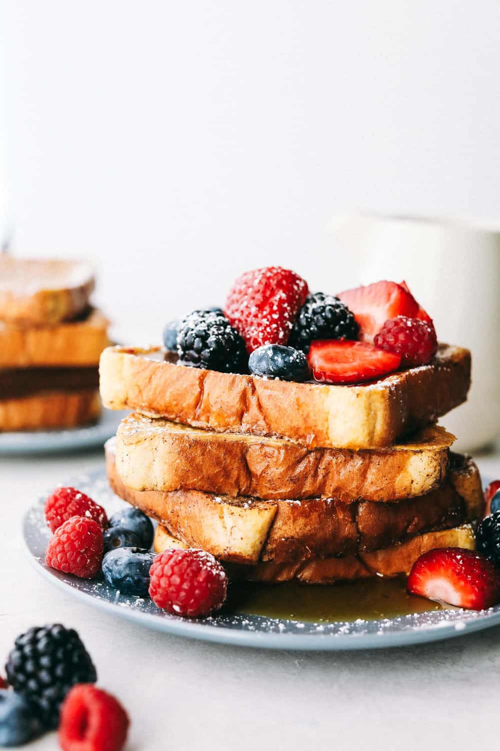 French Toastย is a sliced thick, chunky bread dipped in aย creamy egg, milkย and cinnamon mixture with a secret ingredient that will take thisย French toast over the top! A little slice of heaven on your plate!ย French toast stacked up with berries and powdered sugar on them.