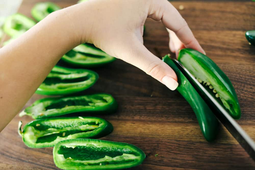 These jalapeรฑoย poppersย are filled with a cream cheese mixture, topped with crumbled bacon pieces, and then baked to perfection. You won't be able to stop at one!ย Slicing jalapeรฑo peppers in half.
