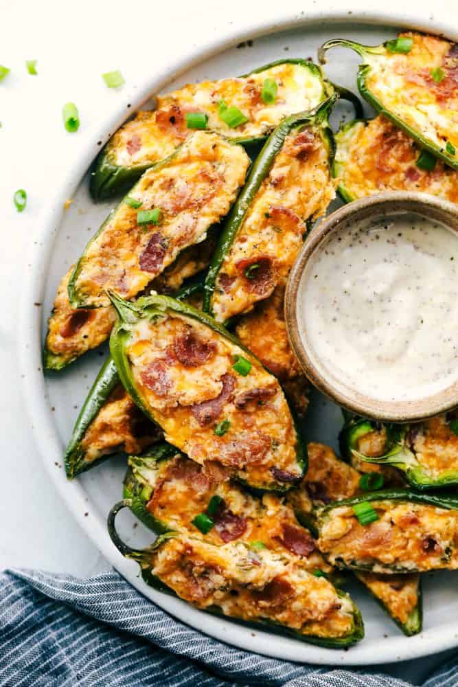 These jalapeรฑoย poppersย are filled with a cream cheese mixture, topped with crumbled bacon pieces, and then baked to perfection. You won't be able to stop at one!ย A platter of jalapeรฑo poppers with some dip.