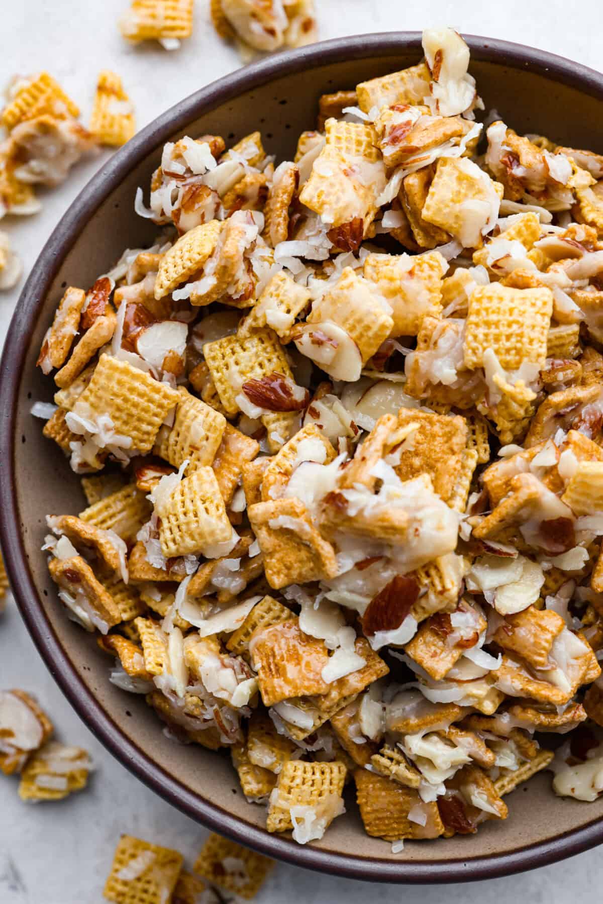 Ooey Gooey Chex Mix is the perfect sweet, salty, and crunchy blend. It has a mixture of cereal, sliced almonds, and shredded coconut, all covered in a soft caramel sugar mixture. This is a must-make for the holiday season! Overhead shot of a bowl of Ooey gooey Chex mix.