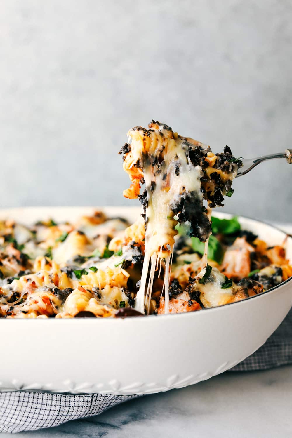 This Turkey Mediterranean Casserole features artichokes, fusilli pasta, sun dried tomatoes and Lindsay® Kalamata Olives baked in a red tomato sauce and topped with Lindsay® Chopped Black Olives. Simple, delicious ingredients in 30 minutes! Turkey Mediterranean casserole in a dish with a fork pulling it away.