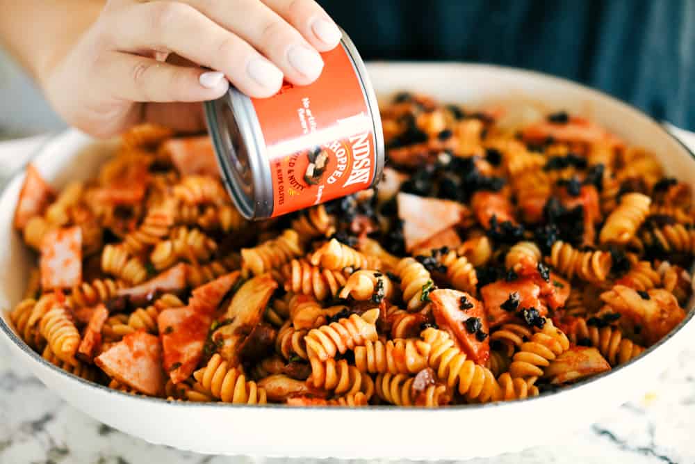 This Turkey Mediterranean Casserole features artichokes, fusilli pasta, sun dried tomatoes and Lindsay® Kalamata Olives baked in a red tomato sauce and topped with Lindsay® Chopped Black Olives. Simple, delicious ingredients in 30 minutes! turkey mediterranean casserole in a dish with Lindsay Olives poured over top.