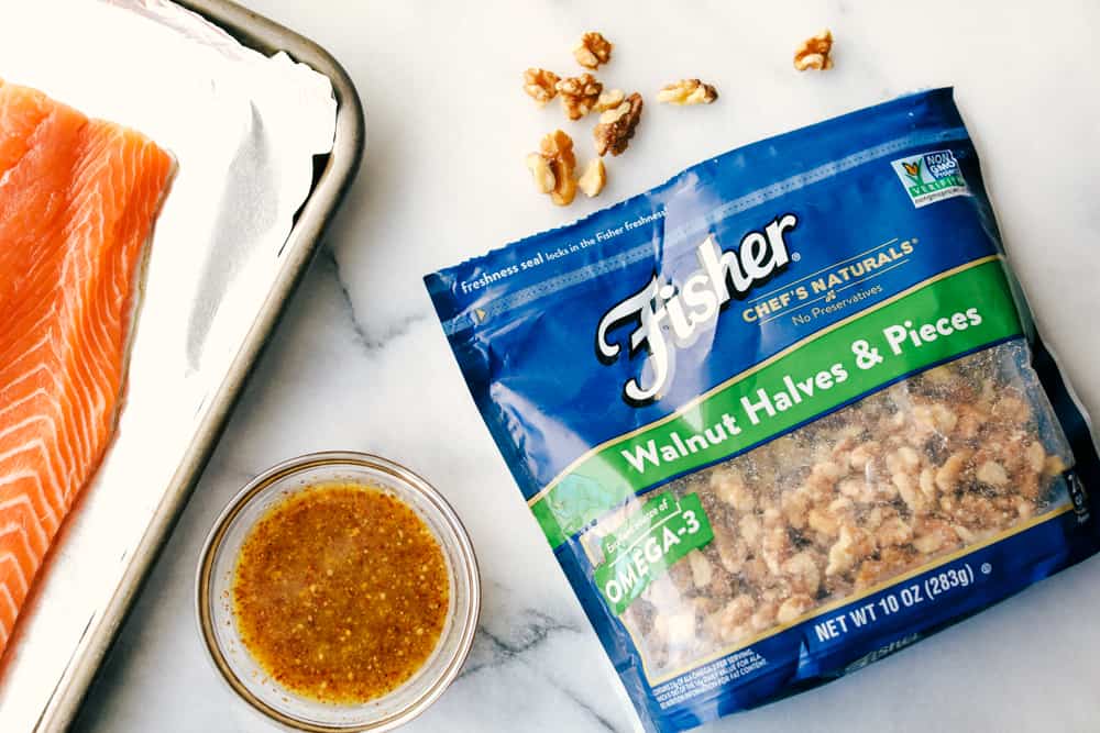 Walnut Crusted Maple Salmon is a savory salmon dish that is coated in a sweet maple syrup, delicious Dijon mustard coated with a thick walnut crust all baked to perfection. Baked in under 30 minutes! fisher walnuts in a bag and salmon with marinated sauce mixture.