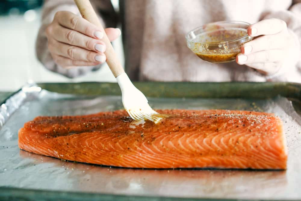 Walnut Crusted Maple Salmon is a savory salmon dish that is coated in a sweet maple syrup, delicious Dijon mustard coated with a thick walnut crust all baked to perfection. Baked in under 30 minutes! A salmon being basted with the marinated sauce.