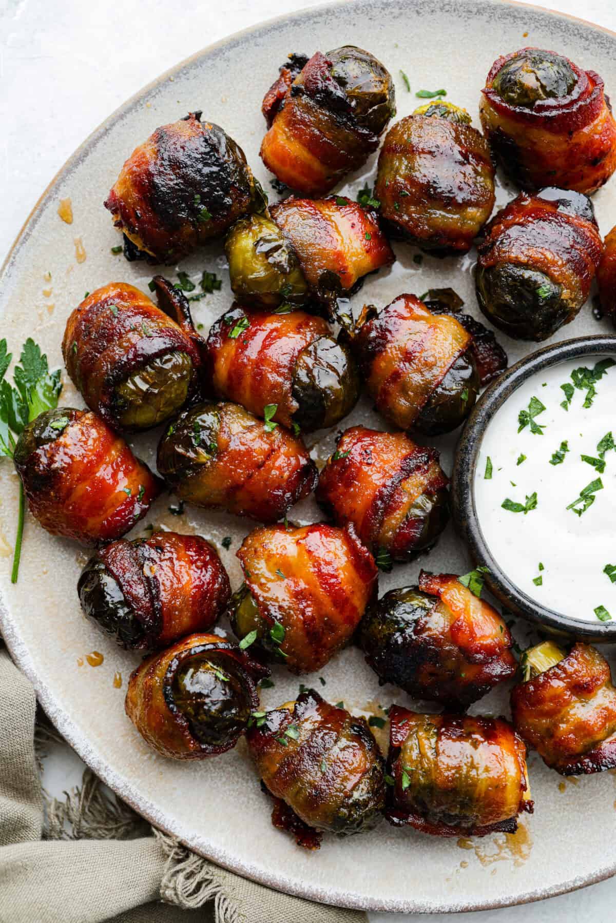 I love bacon. I love Brussels sprouts. Put them together and Iโm sold. But the secret to these bacon-wrapped Brussels sprouts? A drizzle of maple syrup! It makes them sweet, smoky, and completely irresistible. A platter of bacon wrapped Brussels sprouts with some dip.
