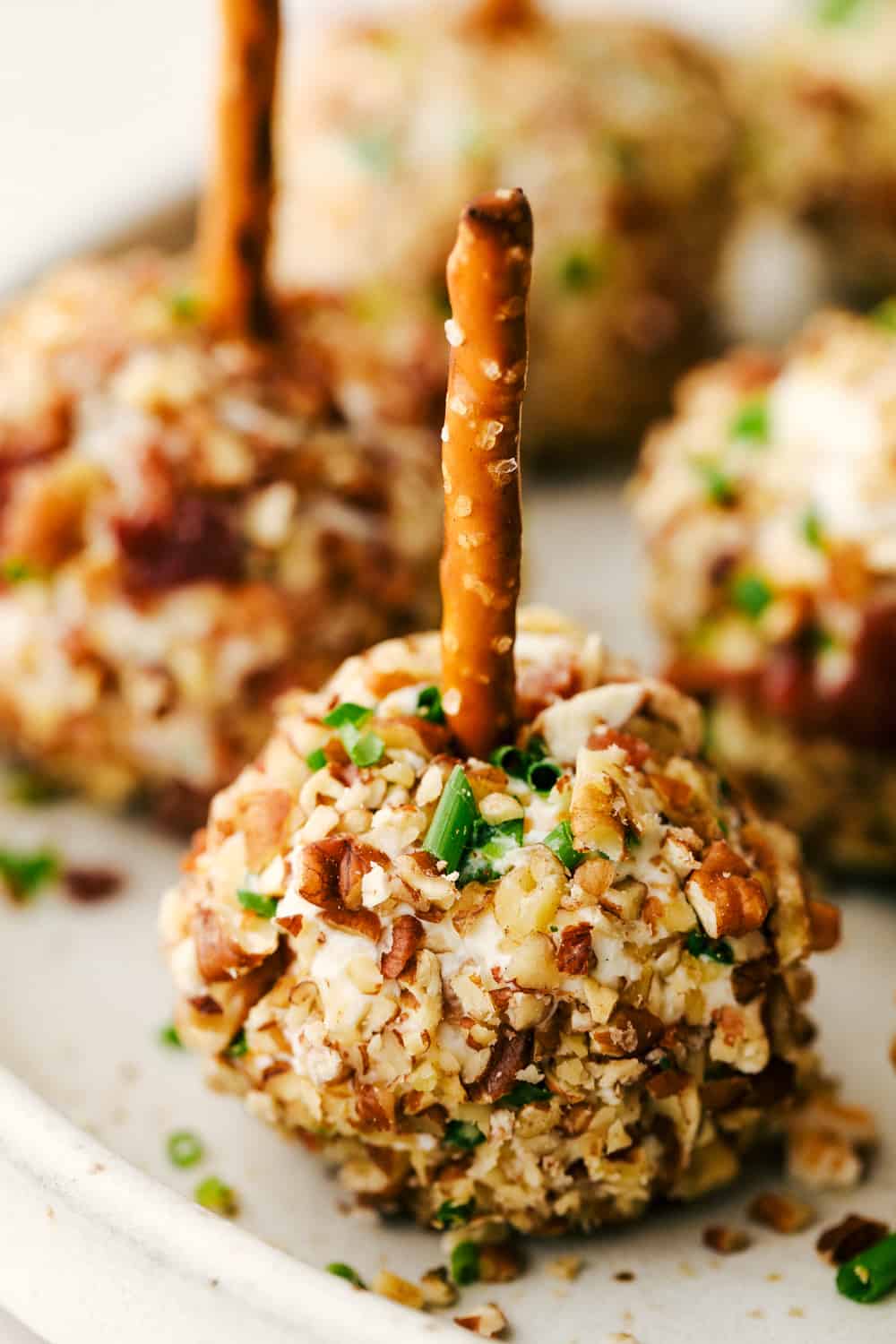 Bacon Ranch Cheese Ball Bites are delicious appetizers loaded with shredded cheese, a pop of color from the green onion, cooked bacon chunks mixed with black olives and pecans all rolled together in a tight ball with a pretzel on top. An elegant appetizer to enjoy this holiday season! Bacon ranch cheese ball bites on a plate.