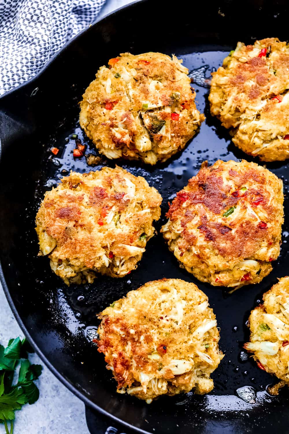 These easy-to-make crab cakes are filled with thick chunks of crab meat mixed togetherย with creamy mayonnaise and sweet red bell pepper, topped off with a kick of red pepperย flakes. The BESTย crab cake recipe you will ever use! Crab cakes on a skillet cooking.