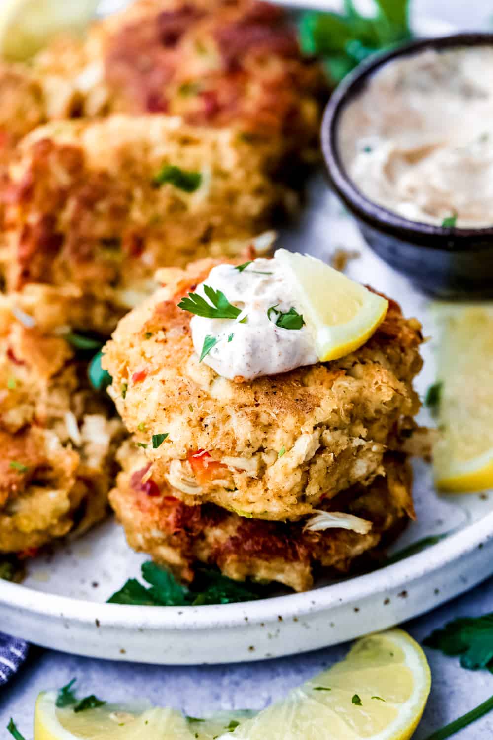 These easy-to-make crab cakes are filled with thick chunks of crab meat mixed togetherย with creamy mayonnaise and sweet red bell pepper, topped off with a kick of red pepperย flakes. The BESTย crab cake recipe you will ever use! Crab cakes on a white plate, topped with tartar sauce.
