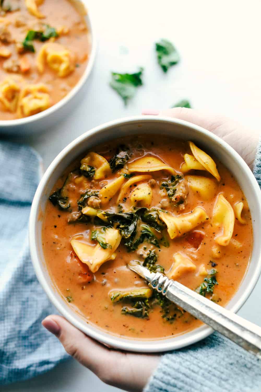 Creamy sausage tortellini soup is thick and creamy with chunks of cooked pork sausage, carrots, buttery kale and three cheese tortellini pasta all cooked in a smooth tomato sauce. This soup will become an instant favorite! Creamy sausage tortellini soup served in a white bowl.