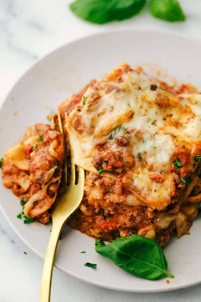 The Best Classic Lasagna Ever has layers of sautéed ground beef and Italian sausage that are cooked together, sweet tomato sauce, Italian seasoning all layered with lasagna noodles then covered in ricotta cheese and a parmesan mixture all sprinkled with mozzarella cheese for a mouthwatering baked Italian dinner. Layers of deliciousness! Lasagna on a plate with a gold fork.