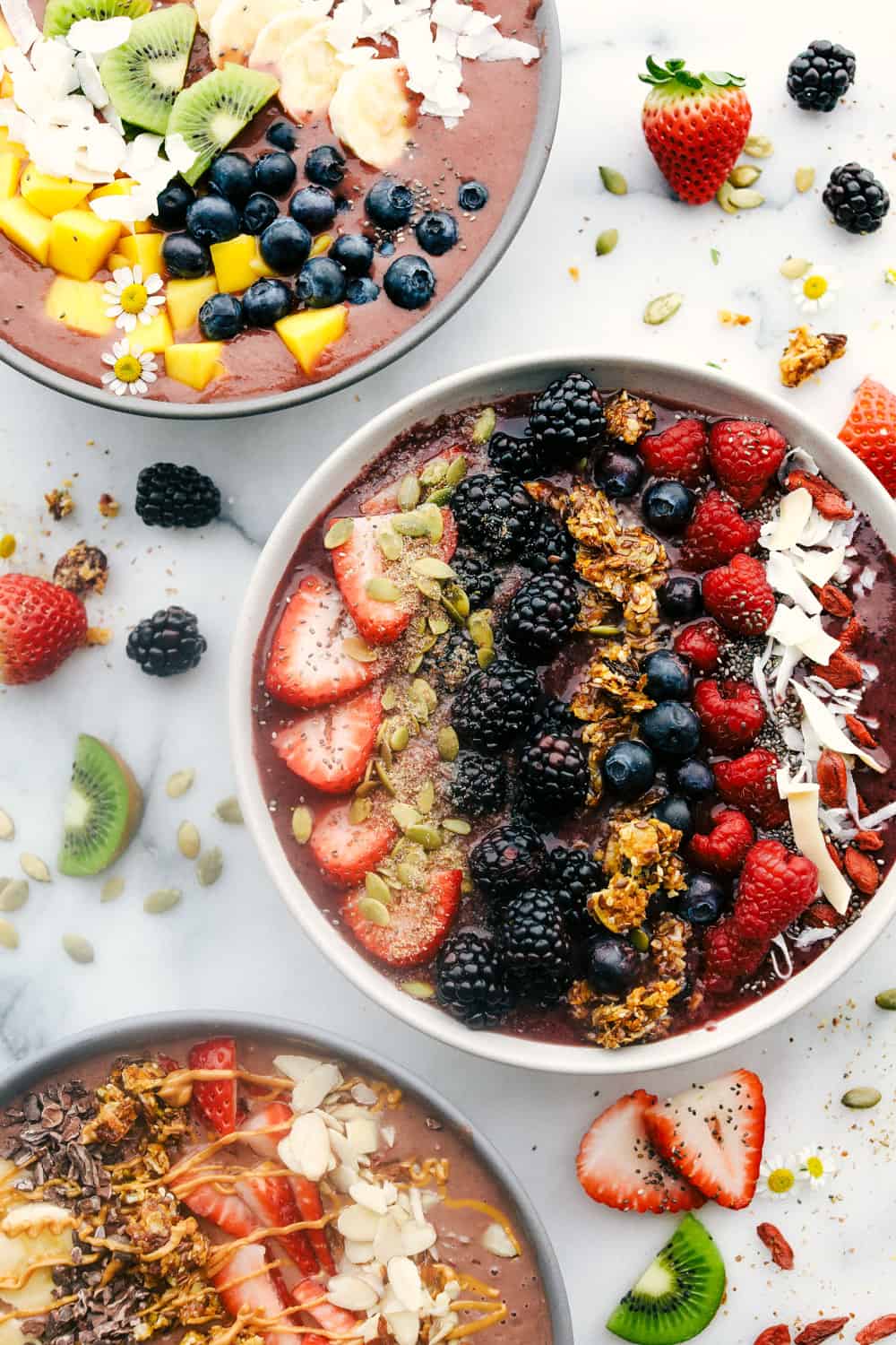 The Best Acai Bowls (Three Ways!) is a fruit filled bowl full of acai berries and juice topped with granola, fresh fruits, crunchy nuts and a variety of seeds all drizzled with a fun topping. A perfect way to start your day or keep it going! Three Acai Bowls with three different flavoring and toppings of fruit and granola.