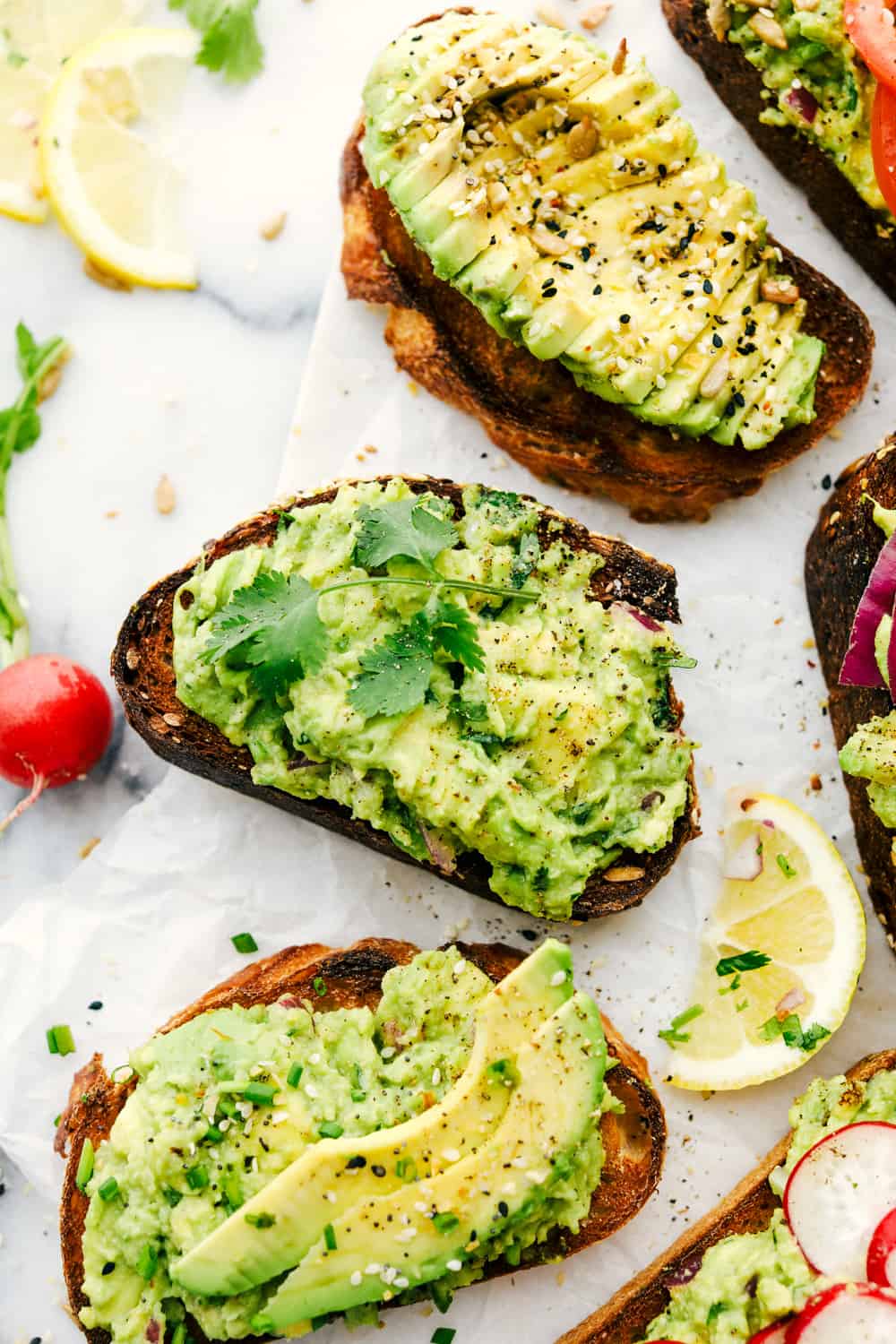 Easy 5 Minute Avocado Toastย is a toasted grain bread with ripe mashed avocados with variations of toppings to make each avocado toast unique and flavorful depending on the time of day. ย Perfect for aย quick breakfast, light lunch or snack! Avocado toast made three different ways with lemon wedges next to them.