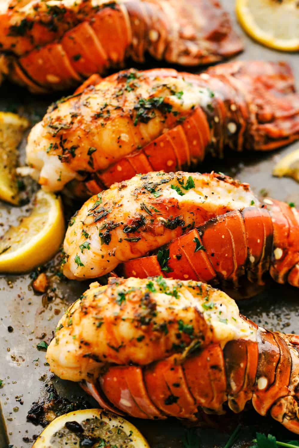 The Best Lobster Tail Recipe Ever is a decadent dinner made with large lobster tails smothered with a buttery garlic herb sauce then broiled under high heat making these lobster tails tender and juicy. The ultimate indulgence! Lobster tails broiled on a sheet pan with lemon slices.