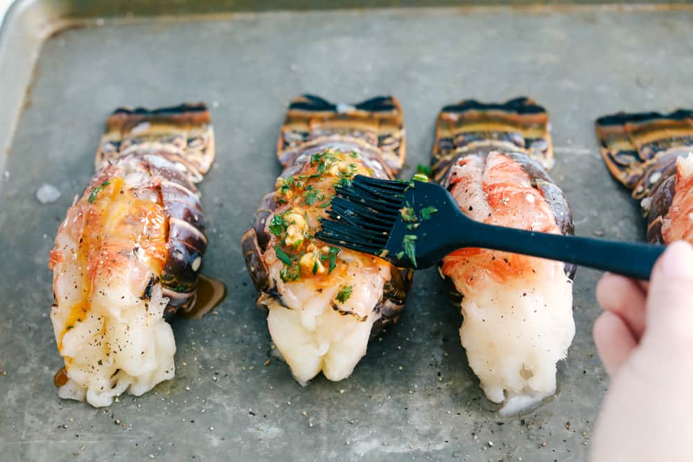 The Best Lobster Tail Recipe Ever is a decadent dinner made with large lobster tails smothered with a buttery garlic herb sauce then broiled under high heat making these lobster tails tender and juicy. The ultimate indulgence! Spreading a buttery garlic herb sauce over top of the lobster tail.