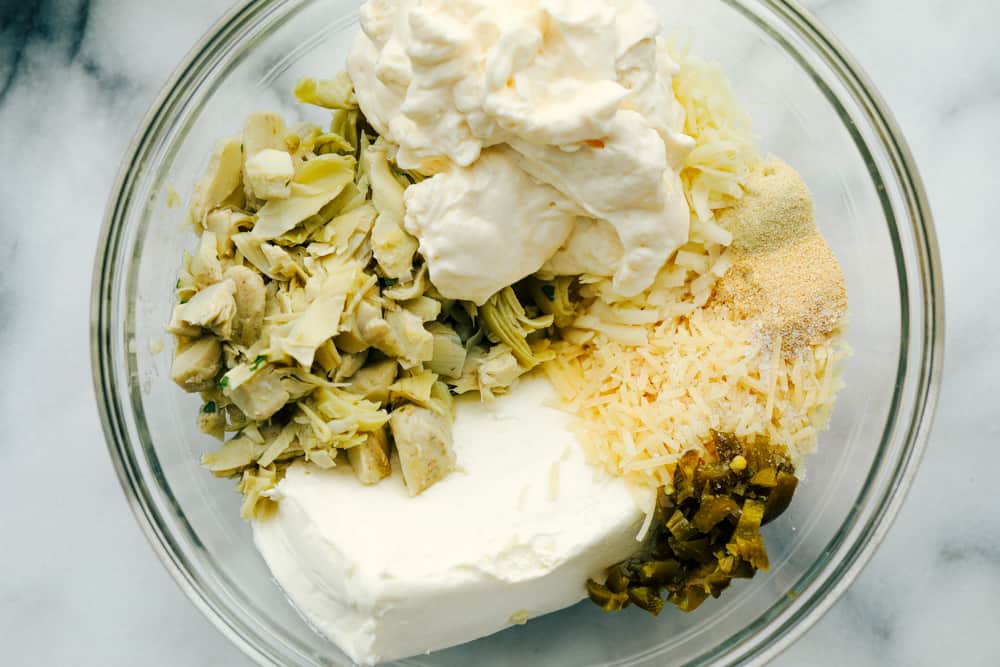 Jalapeño Artichoke Dip is a smooth and creamy blend of cheeses and sour cream mixture with chunks of artichoke hearts and diced jalapeños for a sweet and spicy appetizer dip. This is a MUST try dip for your next party! Jalapeno artichoke dip ingredients in one bowl.