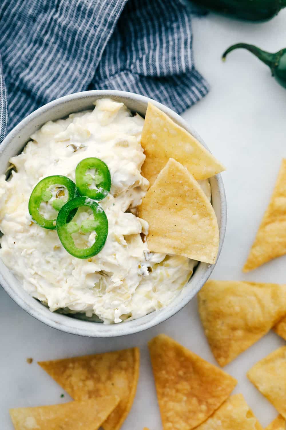 Jalapeño Artichoke Dip is a smooth and creamy blend of cheeses and sour cream mixture with chunks of artichoke hearts and diced jalapeños for a sweet and spicy appetizer dip. This is a MUST try dip for your next party! Jalapeño artichoke dip in a bowl with jalapeños garnished on top with chips for dipping.