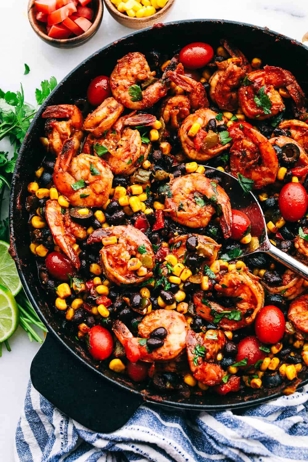 Mexican Shrimp Skillet is full of thick, plump shrimp with black beans, goldenย yellowย corn, ripe cherry tomatoes, chopped bell peppers, black olives mixedย together in myย famous tacoย seasoning all inย sautรฉd in one pan. All under 20 minutes! Mexican shrimp skillet in a skillet with a spoon.