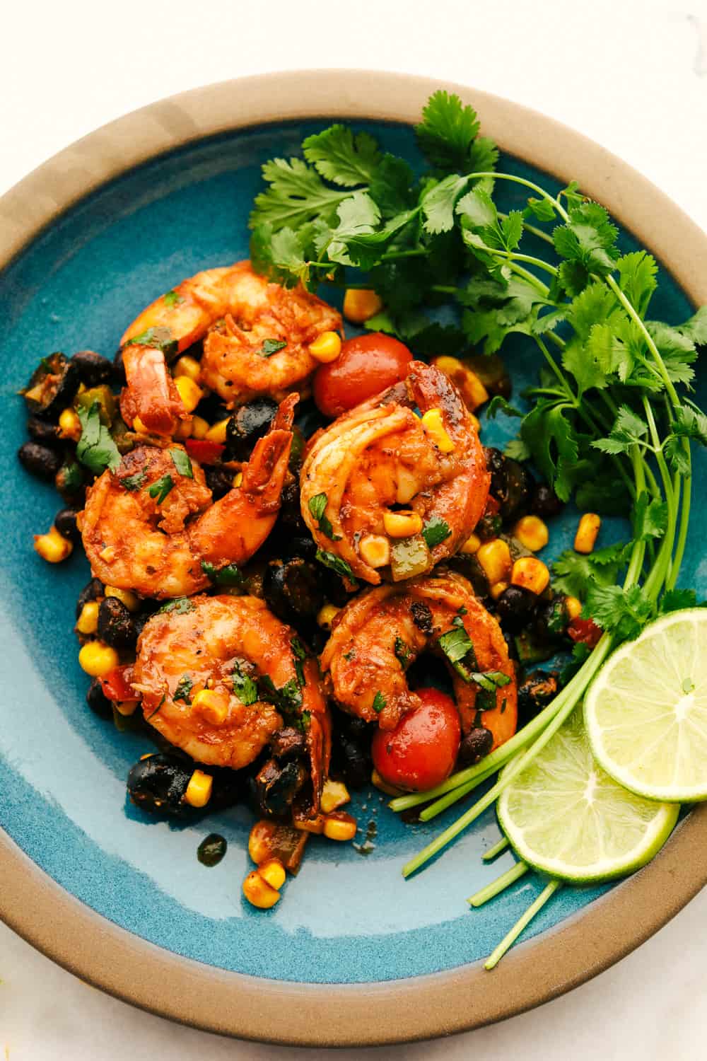 Mexican Shrimp Skillet is full of thick, plump shrimp with black beans, goldenย yellowย corn, ripe cherry tomatoes, chopped bell peppers, black olives mixedย together in myย famous tacoย seasoning all inย sautรฉd in one pan. All under 20 minutes! Mexican shrimp skillet served on a plate.