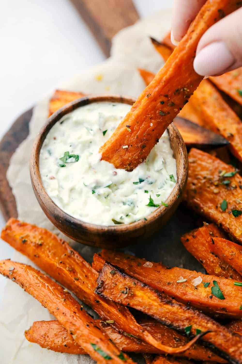 Crispy Garlic Sweet Potato Fries are thick cut sweet potatoes baked in olive oil and then seasoned with garlic powder and Italian seasoning for a crispy outside and a tender inside. The perfect side dish or snack! Crispy garlic sweet potatoes being dipped in the avocado ranch dipping sauce.