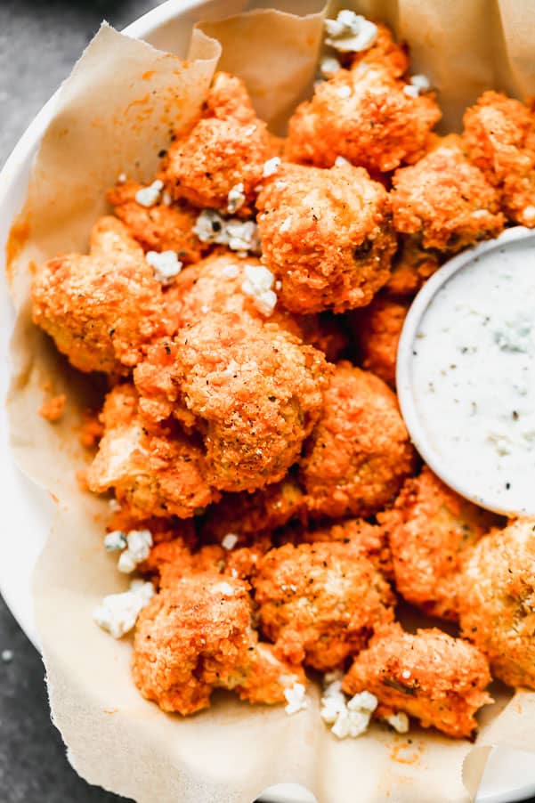 Buffalo Cauliflower takes all your favorite things about buffalo chicken wings - the crispy exterior, soft interior, and tangy, spicy buffalo taste - and turns them into a healthier option you don't have to feel guilty about eating. Super easy and so good! Buffalo cauliflower in a bowl with ranch dip on the side.