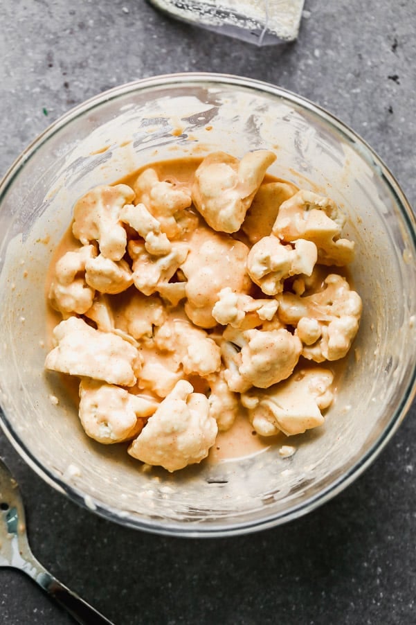 Buffalo Cauliflower takes all your favorite things about buffalo chicken wings - the crispy exterior, soft interior, and tangy, spicy buffalo taste - and turns them into a healthier option you don't have to feel guilty about eating. Super easy and so good! Cauliflower mixed in buffalo sauce in a bowl.