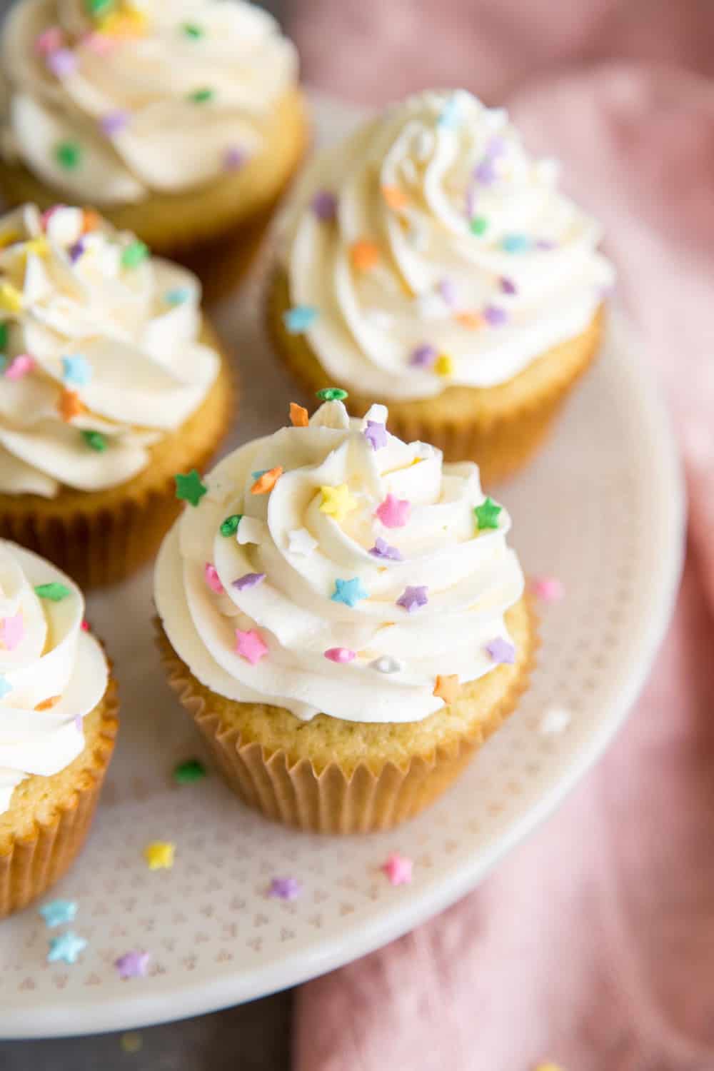 Easy Vanilla Cupcakes with vanilla frosting are such a classic treat for birthdays and perfect for any celebratory occasions. These moist cupcakes with their creamy crown of frosting will surely bring a smile to your face! Vanilla cupcakes on a cake stand