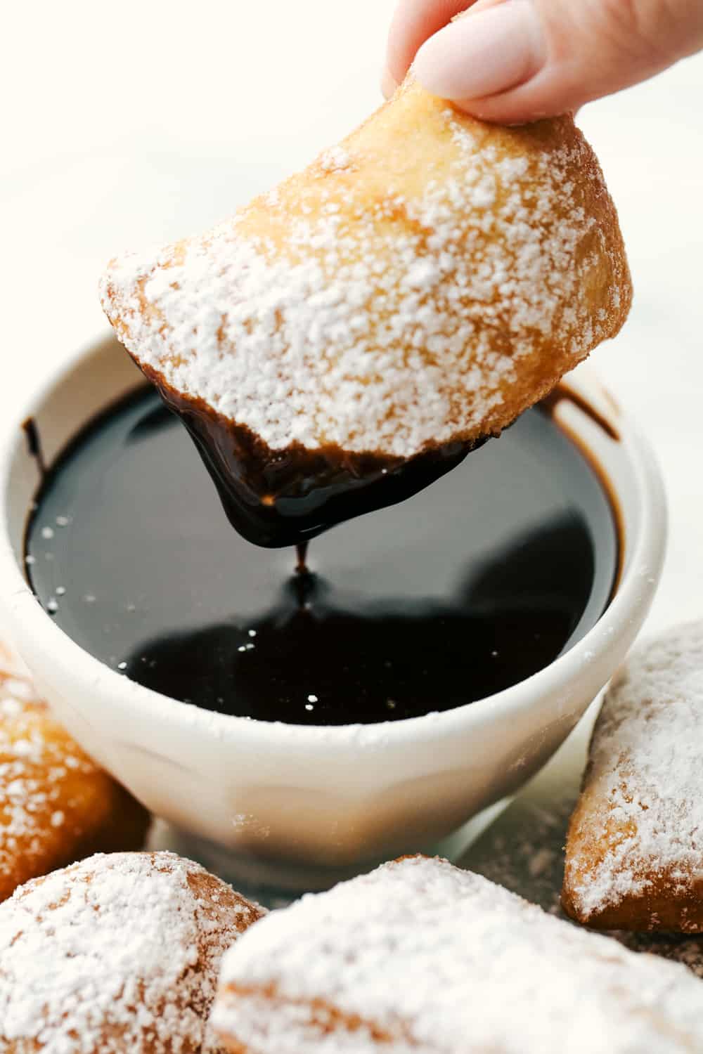 Best Beignets Recipe is a light, fluffyย Frenchย doughnut that are cut into squares and puffed up when fried in oil and then end by sprinkling with powdered sugar or dipped inย chocolate syrup. The best pillowy-soft and fluffy treat to enjoy!ย A beignet covered in powder sugar then being dipped in chocolate syrup.