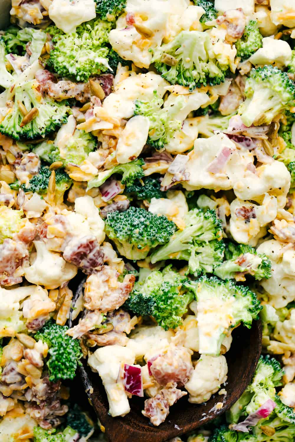 Cauliflower broccoli salad is filled with fresh florets and red onions, bacon pieces with chunks of cheese making this the perfect side salad. Cauliflower broccoli salad photo with shredded cheese and bacon shown throughout.