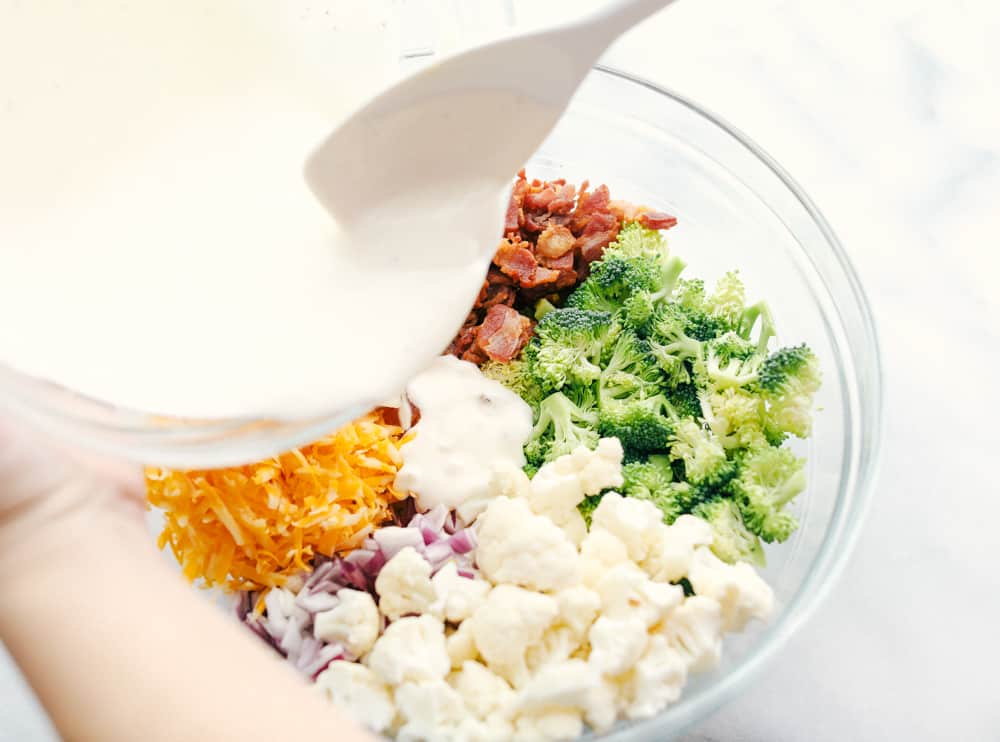 Cauliflower broccoli salad is filled with fresh florets and red onions, bacon pieces with chunks of cheese making this the perfect side salad. All the ingredients chopped up with the mayonnaise dressing being poured overtop.