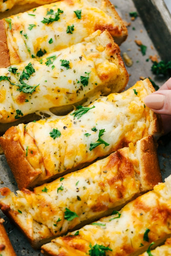 Cheesy garlic bread is so simple to make with loads of cheese and that soft bread on the inside with the crunchy crust on the outside. This is a family favorite for sure!ย Cheesy garlic bread on a pan being pulled apart.